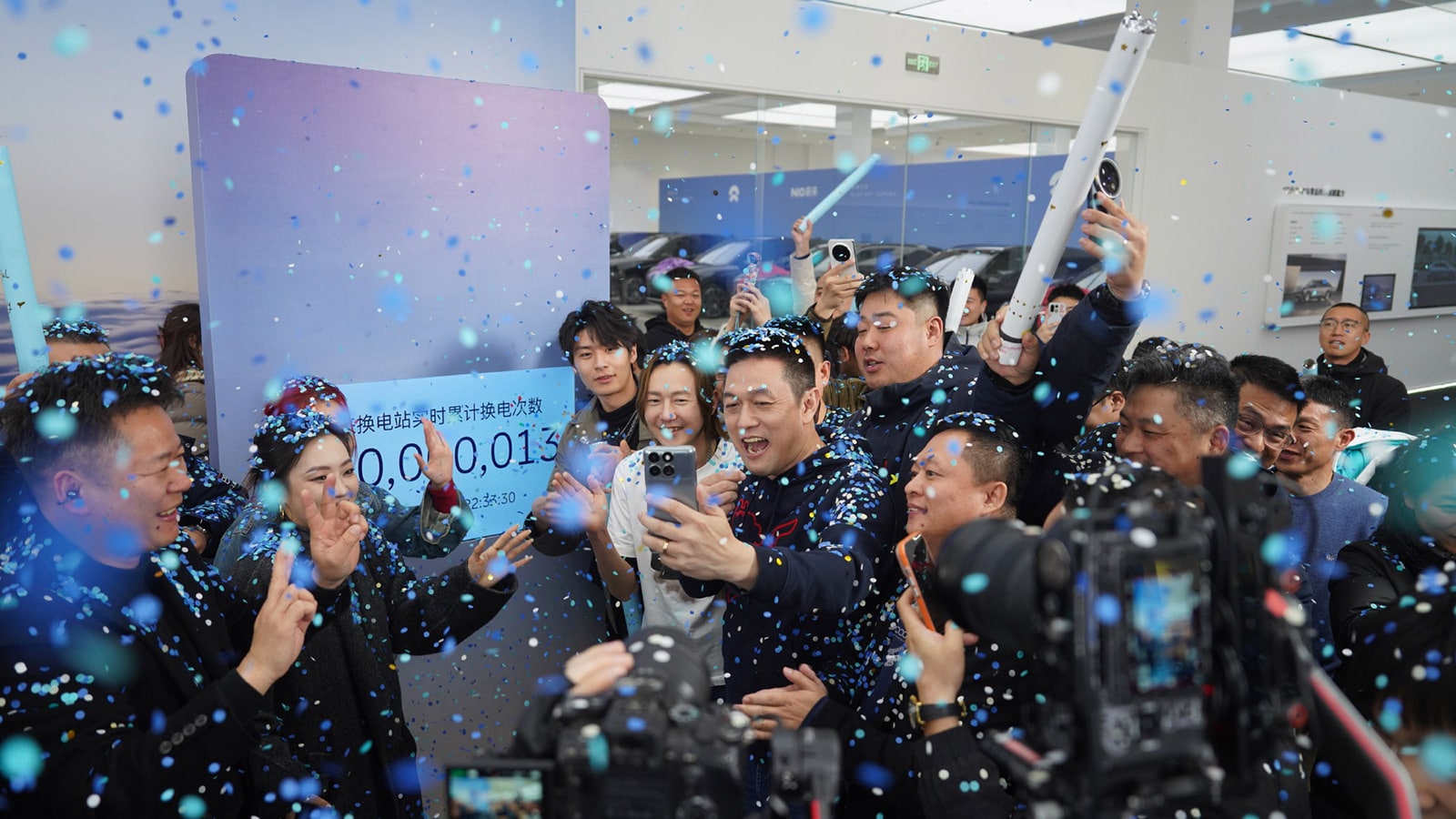 Nio founder, chairman, and CEO William Li (center, holding phone) celebrates the company's 100 millionth battery swap service milestone with Nio owners, partners, and his team.